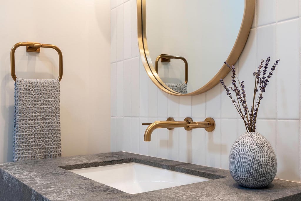 Modern bathroom vanity from a home renovation in South Cambie featuring a grey stone countertop, integrated white sink, brushed gold wall-mounted faucet, and a round gold-framed mirror