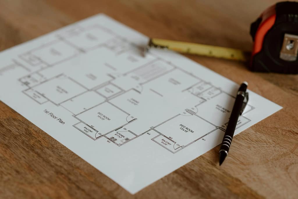 First floor architectural plan for a home renovation project with a measuring tape and pen on a wooden surface.