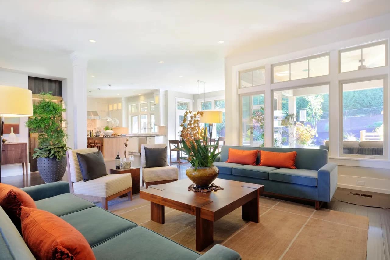 Large living area with blue and green couches, large plants, a wooden coffee table and lots of windows