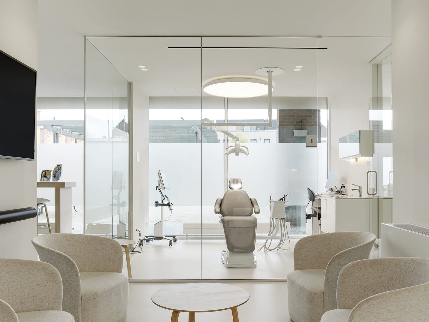 A luxury dental office renovation in Vancouver by Quay Construction featuring a glass-enclosed treatment room, ergonomic patient chair, and a minimalist neutral waiting area.