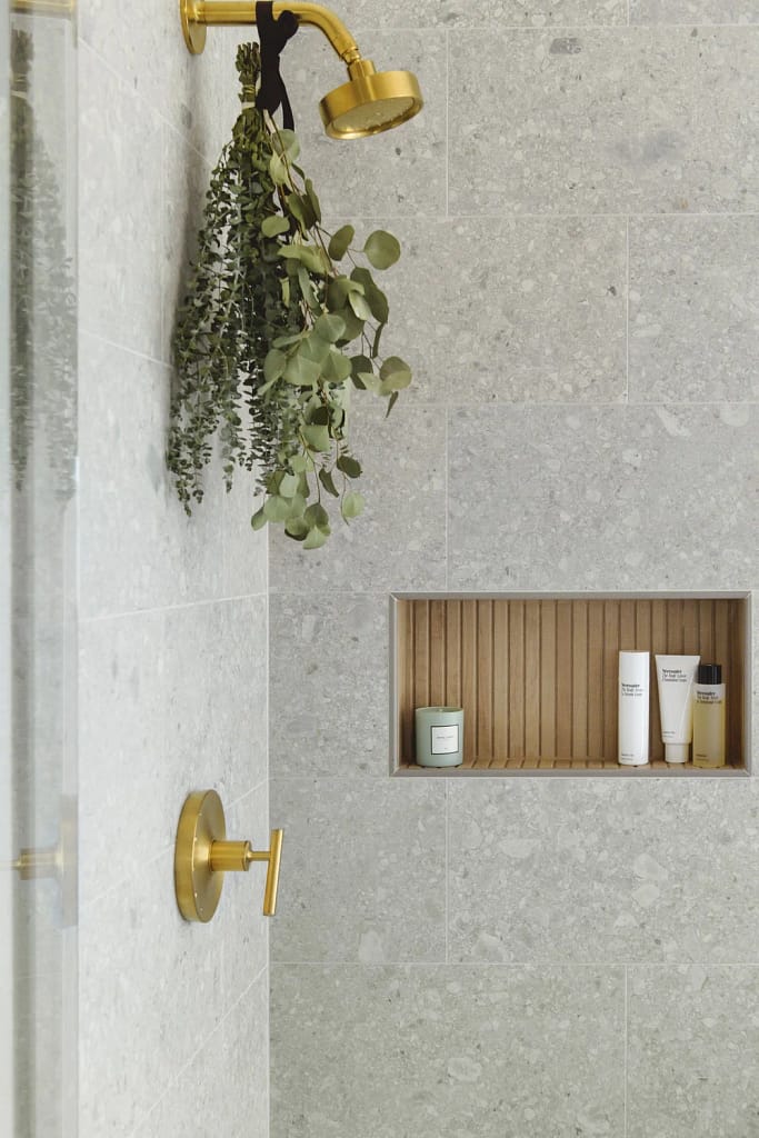 Luxury shower detail by Quay Construction featuring grey terrazzo wall tiles, a built-in oak wood niche, and brushed gold fixtures.