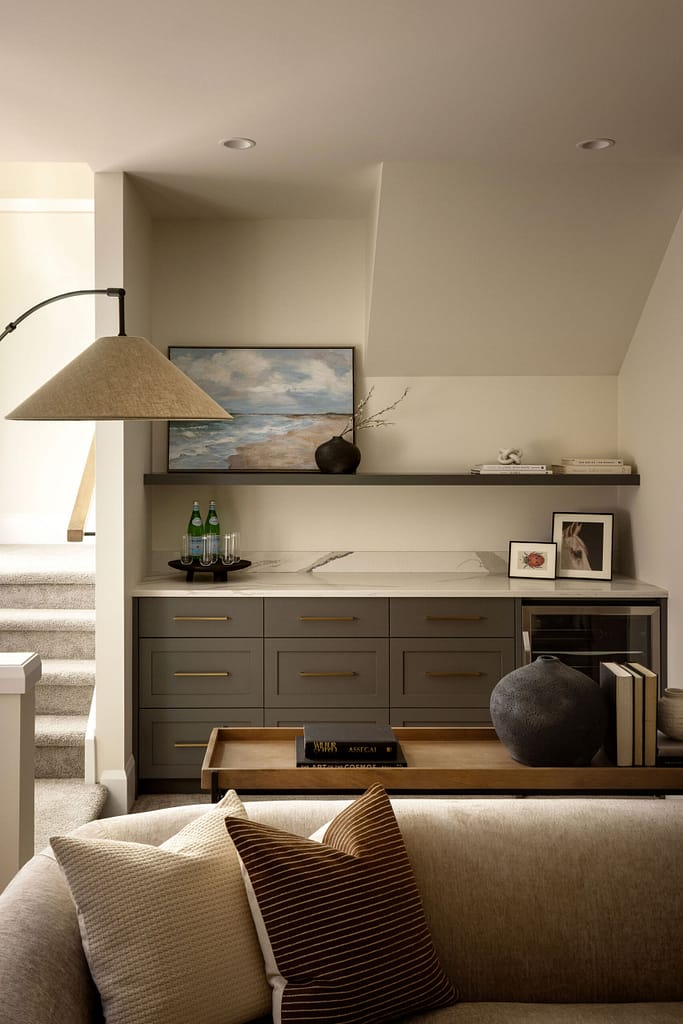 Modern basement wet bar with grey cabinetry, gold hardware, and marble countertop built under a staircase by Quay Construction.