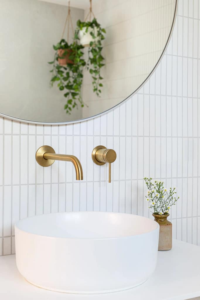 Modern bathroom improvement by Quay Construction featuring a white vessel sink, brushed gold wall-mounted faucet, and vertical white stack bond tile.