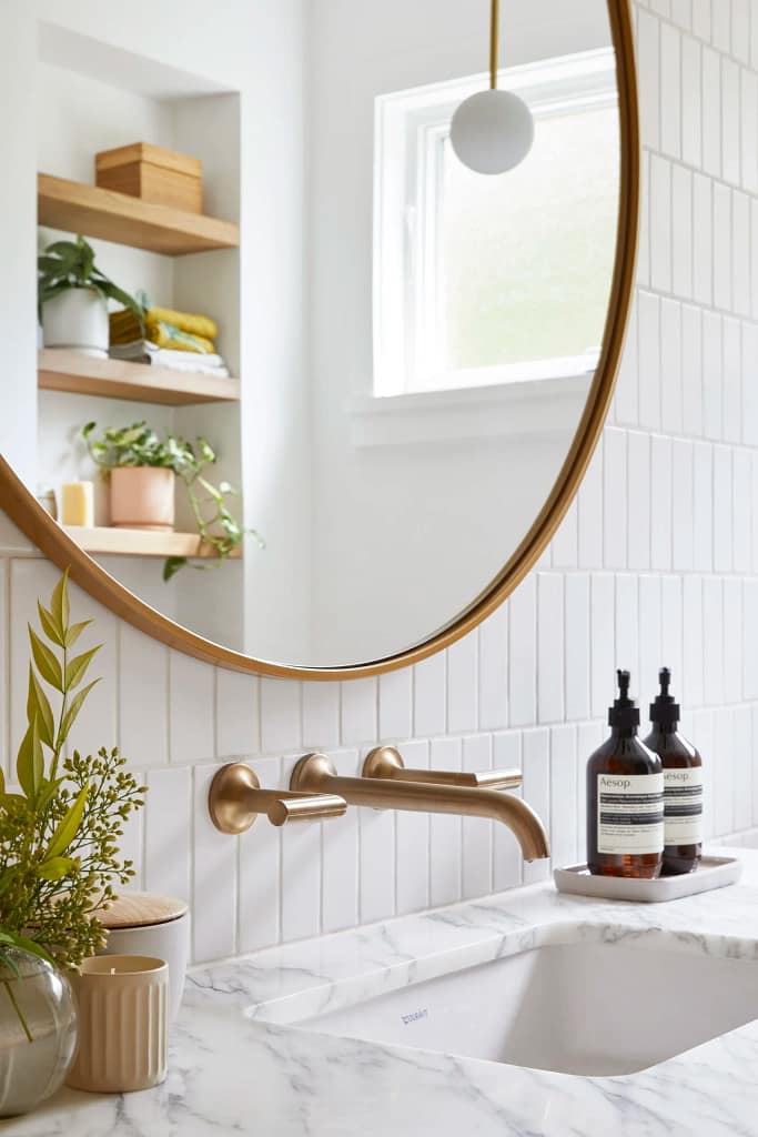 A luxury bathroom renovation in City Centre, Richmond, featuring a gold wall-mounted faucet, white vertical tiles, and a marble countertop.