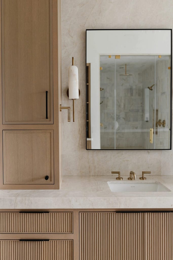 Modern bathroom vanity with fluted wood cabinets and marble countertops from a luxury home renovation in Broadmoor by Quay Construction.
