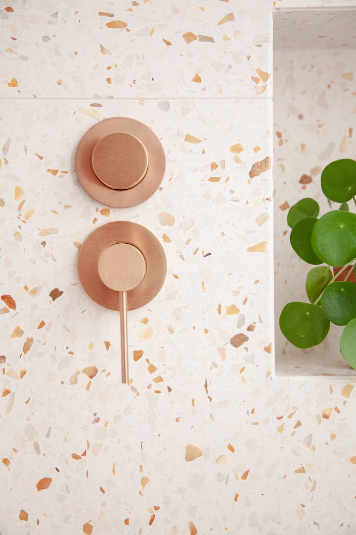 Close-up of modern brushed gold shower controls mounted on a warm-toned terrazzo tile wall from a bathroom renovation in Richmond by a professional contractor.