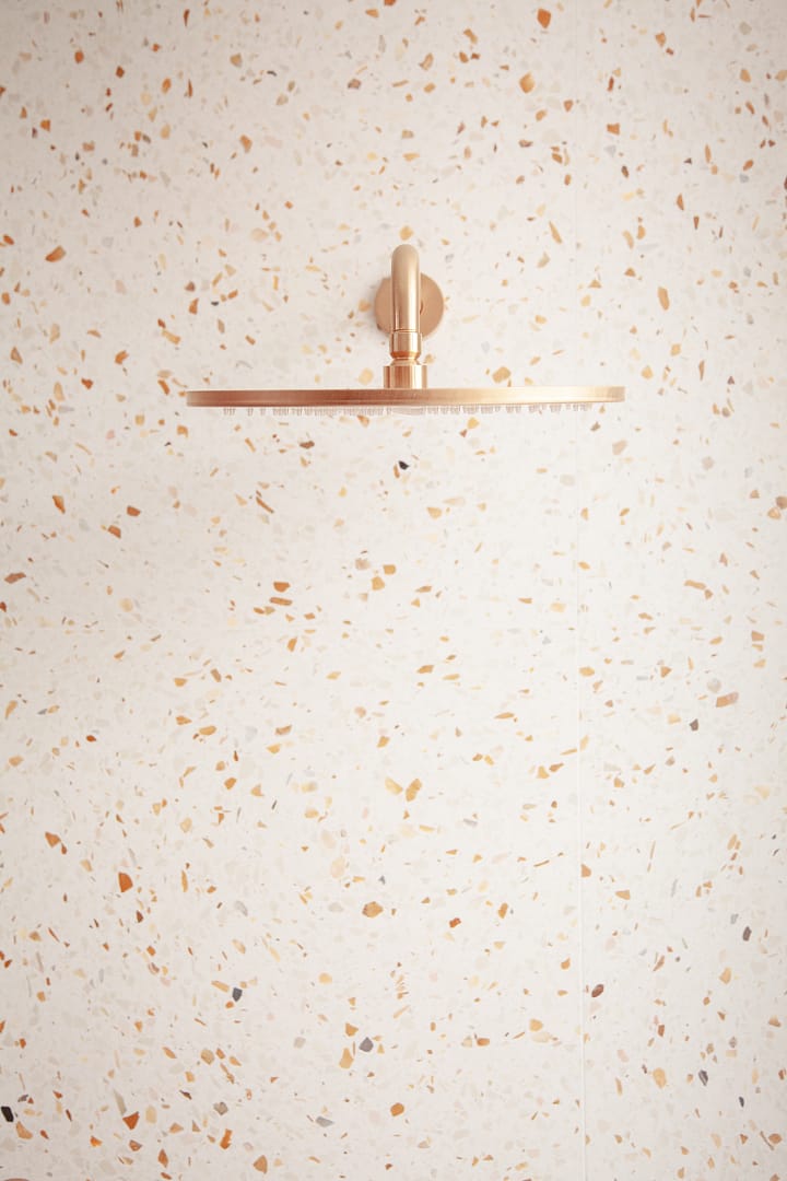 Modern gold rain shower head mounted on a light-colored terrazzo tile wall as part of a bathroom renovation in Richmond by a professional contractor.