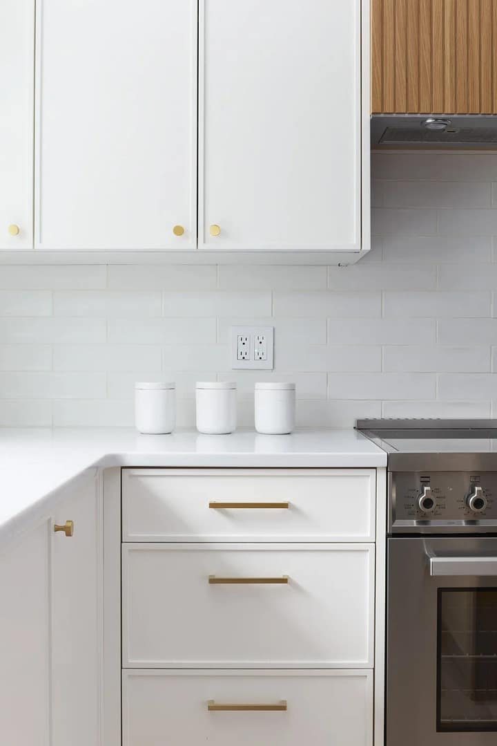 Full view of a Surrey kitchen renovation featuring a large island with wood stools, sage green cabinetry, white Zellige tile backsplash, and a custom arched wood pantry door.