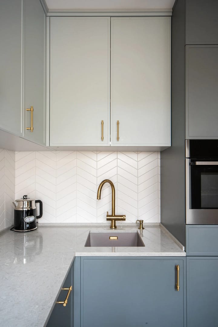 Modern kitchen renovation in North Vancouver by Quay Construction featuring blue and grey custom cabinetry, white chevron backsplash, and brushed gold fixtures.