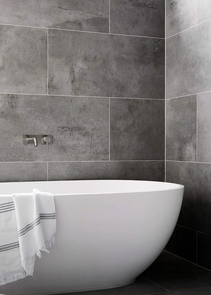 Luxury bathroom renovation by Quay Construction featuring a white freestanding soaking tub against dark grey marble-style large format wall tiles.