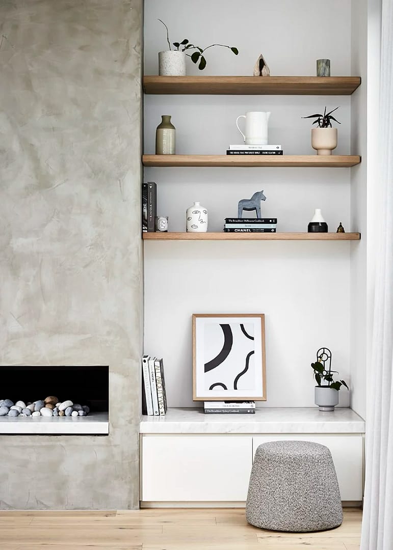 A modern living room from a home renovation in Renfrew–Collingwood featuring a concrete-finish fireplace, custom oak floating shelves, and minimalist white cabinetry.