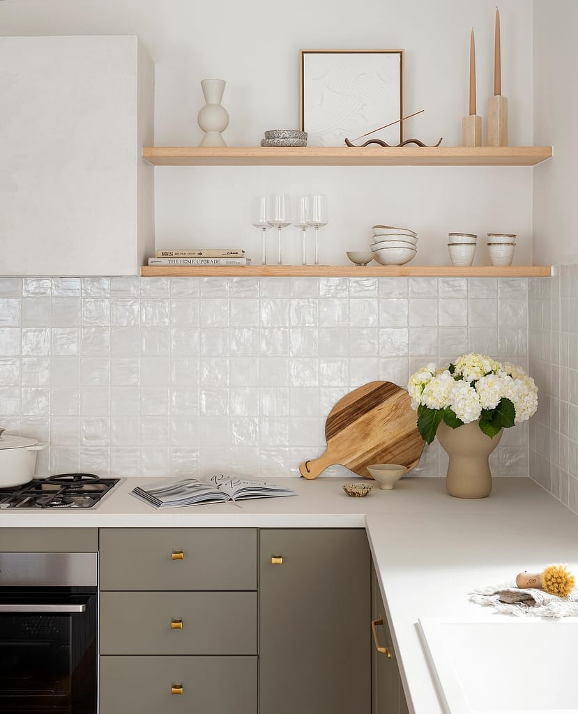 Modern home renovation in Central Lonsdale by Quay Construction featuring a luxury kitchen with a large waterfall island, minimalist white cabinetry, and gold pendant lighting.