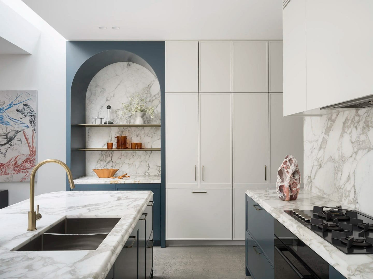 A luxury kitchen from a home renovation in Coquitlam by Quay Construction featuring a marble-lined arched alcove with blue cabinetry and white shaker-style storage.