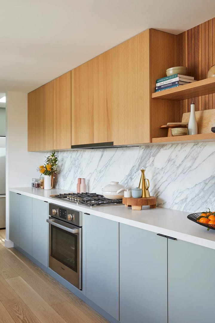 Modern kitchen renovation by Quay Construction featuring two-toned blue base and oak upper cabinets, a marble backsplash, and built-in Bosch appliances.