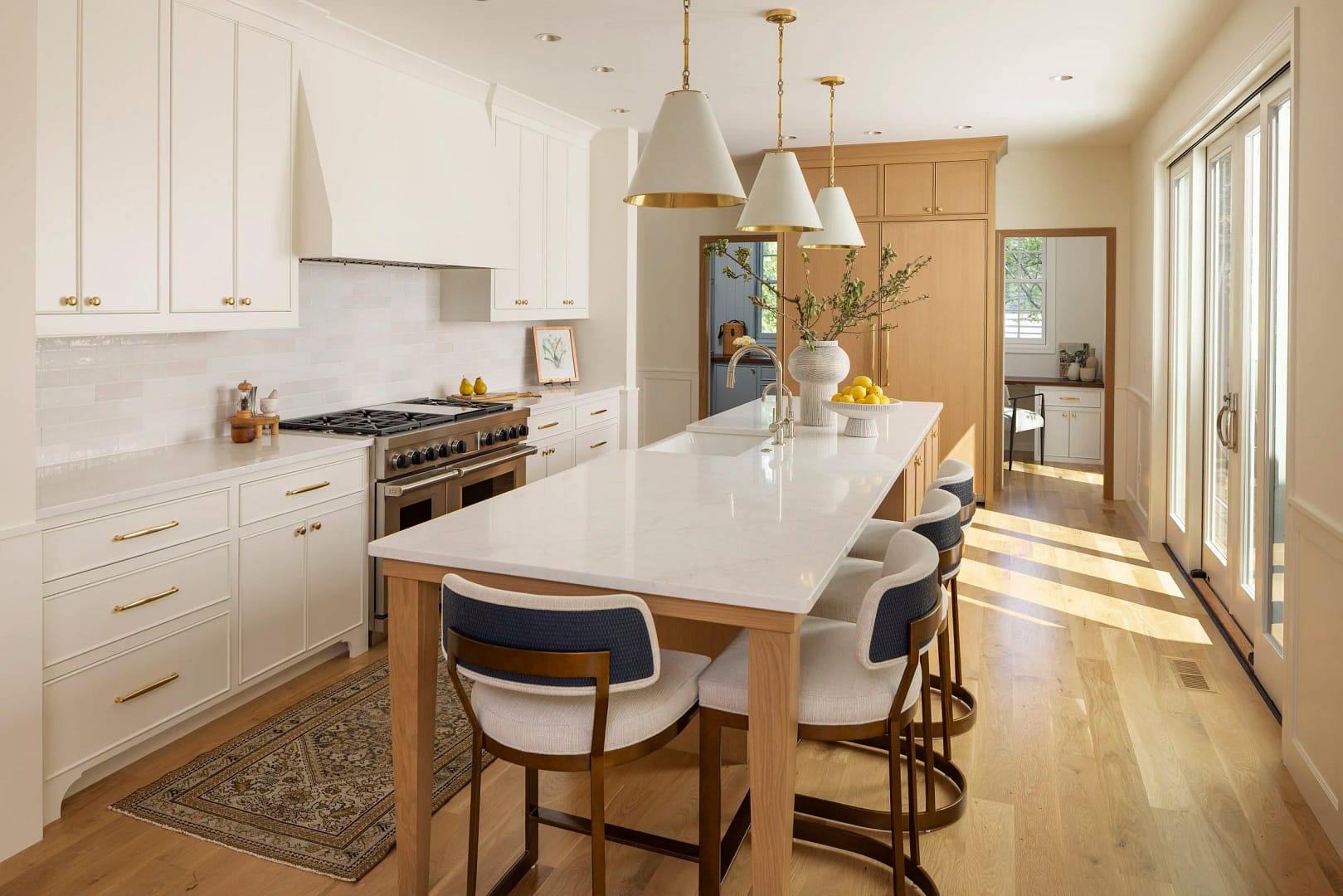 A luxury home renovation in Vancouver by Quay Construction featuring a large white quartz kitchen island with gold pendant lighting, custom cream cabinetry, and light oak hardwood flooring.