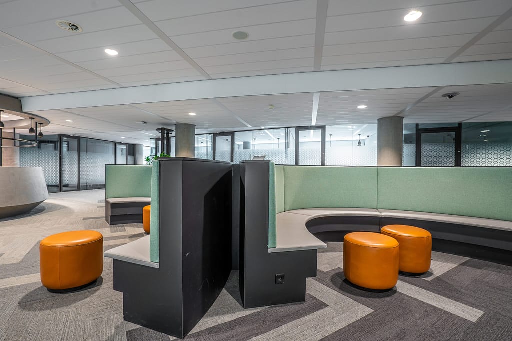 a room with a large round couch and orange stools
