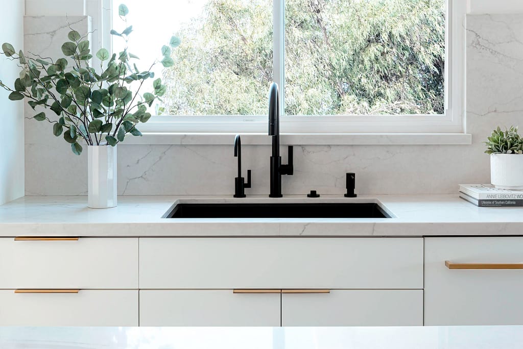 Modern kitchen from a home renovation in Dunbar–Southlands featuring a black undermount sink, matte black faucets, white quartz countertops, and minimalist cabinetry with gold hardware.