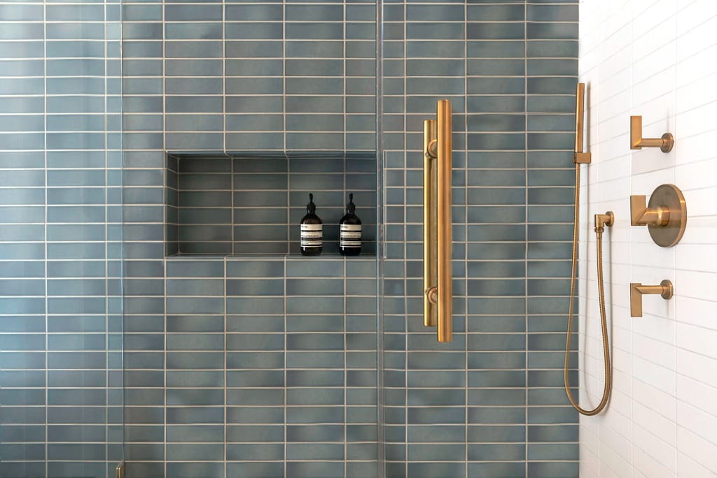 Modern walk-in shower from a home renovation in Renfrew–Collingwood featuring blue vertical stack bond tiles, a recessed shower niche, and luxury brushed gold fixtures.