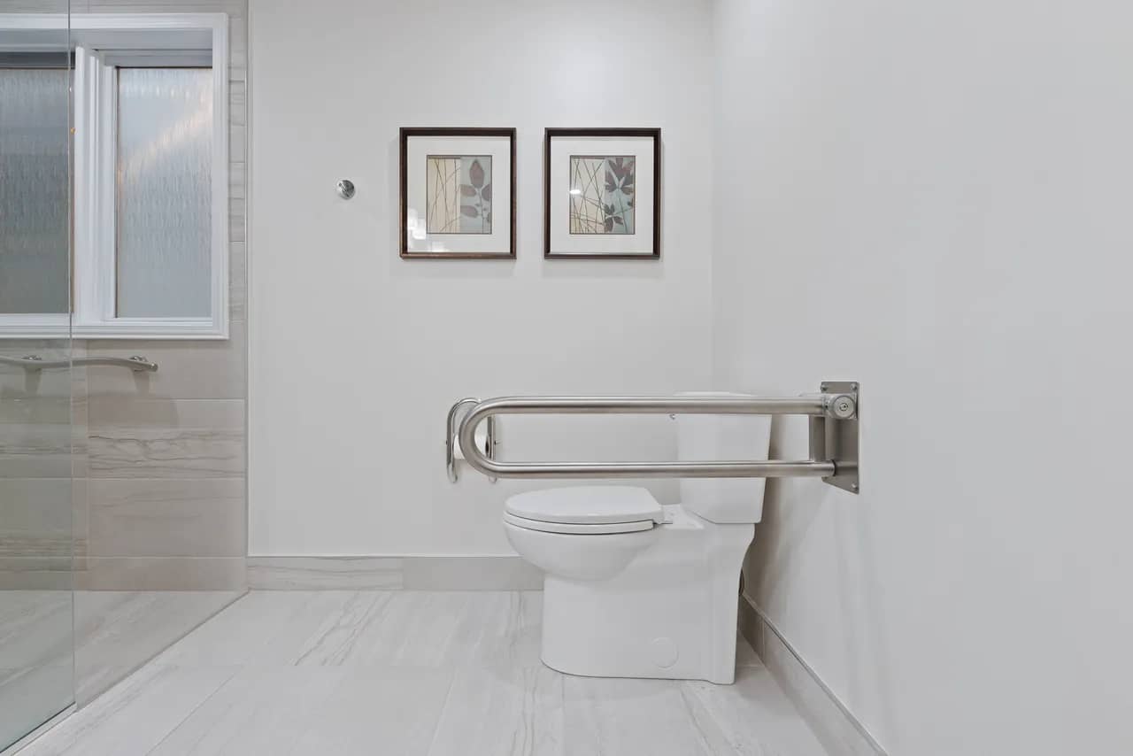 Spacious residential washroom, grab bar, white toilet, marble tile