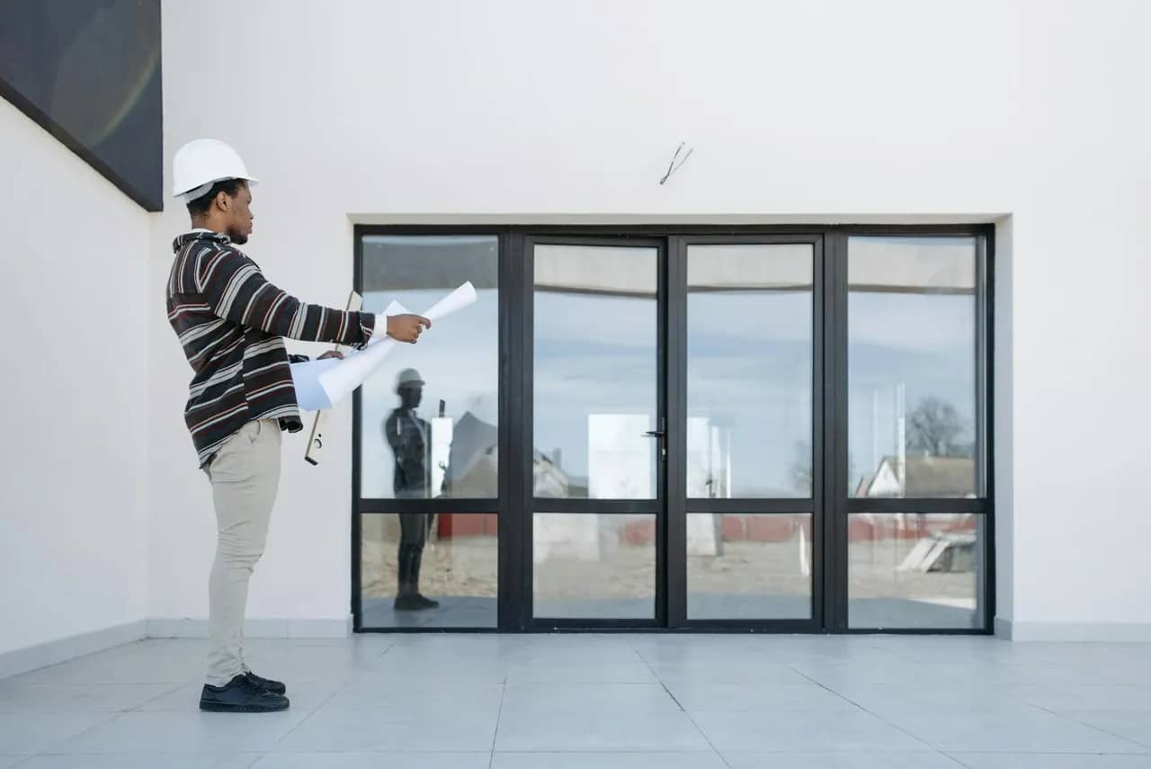 A construction worker standing in front of a glass door looking at his plan