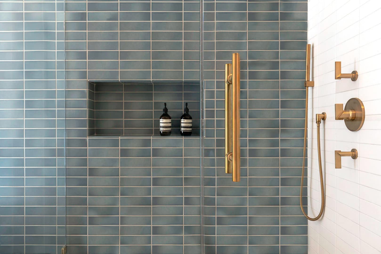 A modern walk-in shower from a basement renovation in Vancouver featuring slate blue subway tiles, a built-in shower niche, and premium brushed gold hardware.