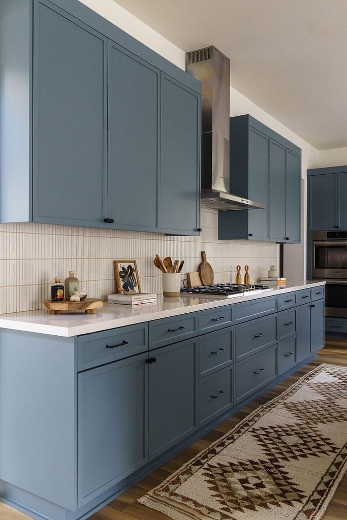 Burke Mountain kitchen renovation with modern blue shaker cabinets, long white subway tile backsplash, stainless steel range hood, and white quartz countertop.