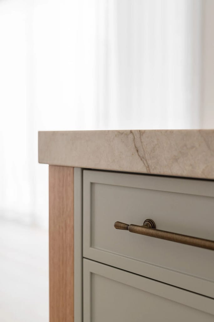 Close-up of a West Vancouver kitchen renovation featuring light sage shaker cabinets, brass hardware, and a thick marble countertop.
