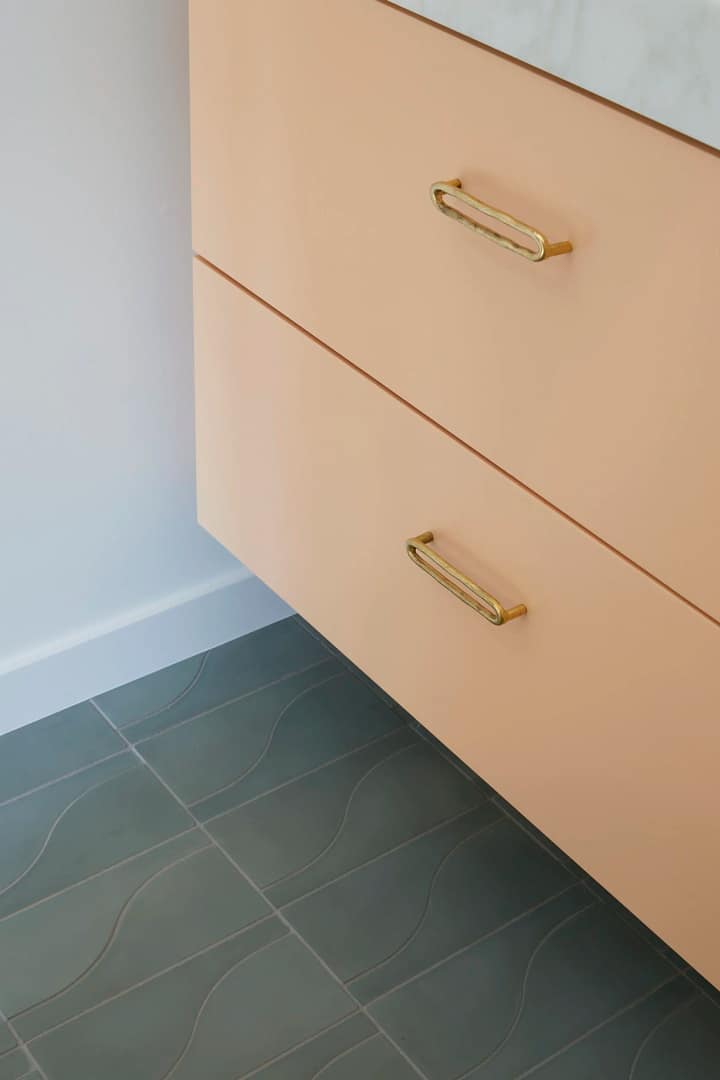 Contemporary basement renovation in Burnaby featuring a peach-colored floating vanity with gold hardware and teal wavy floor tiles by QUAY Construction.
