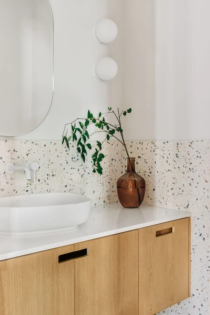 Modern bathroom renovation in Burnaby featuring a white vessel sink on an oak vanity with a colorful terrazzo backsplash by Quay Construction.