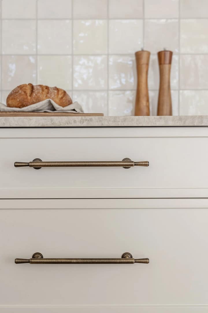 Detail of modern white kitchen cabinetry from a home renovation in Renfrew–Collingwood featuring elegant brass handles and a white zellige tile backsplash.
