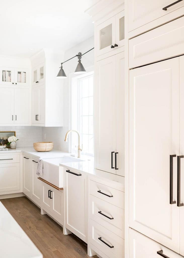 Classic Coquitlam kitchen design featuring white shaker cabinets, a white apron-front farmhouse sink, matte black hardware, and a panel-ready integrated refrigerator.