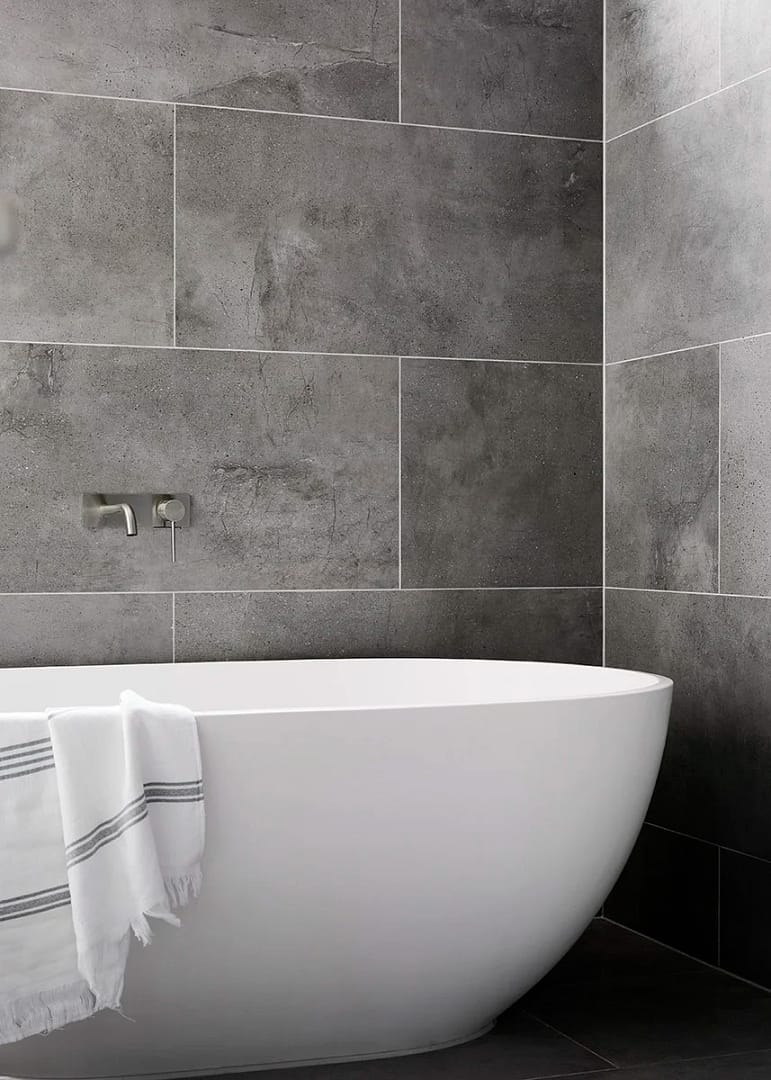 A modern white freestanding soaking tub against a dark grey stone tile wall with a minimalist silver tub filler from a home renovation in Dunbar–Southlands.
