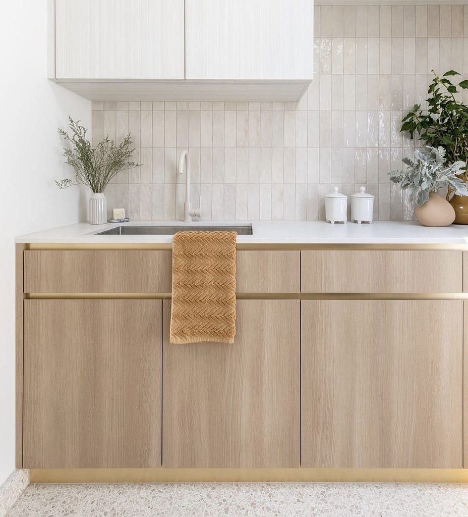 Modern kitchen renovation in Coquitlam featuring light wood lower cabinets, white upper cabinets, a subtle vertical tile backsplash, and elegant brass hardware, demonstrating cost options for kitchen remodels.