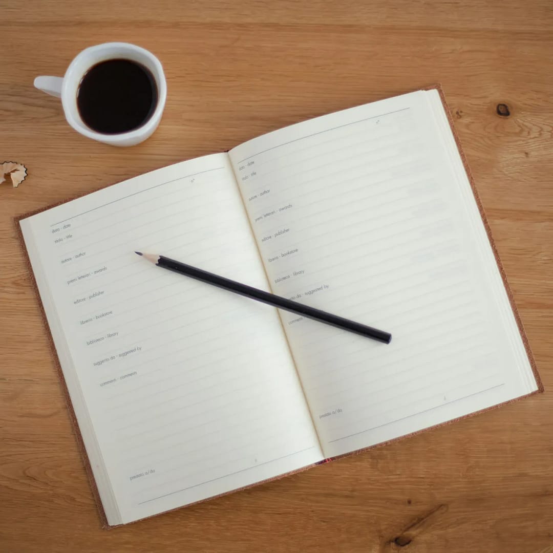 a pencil on a notebook beside a cup of coffee