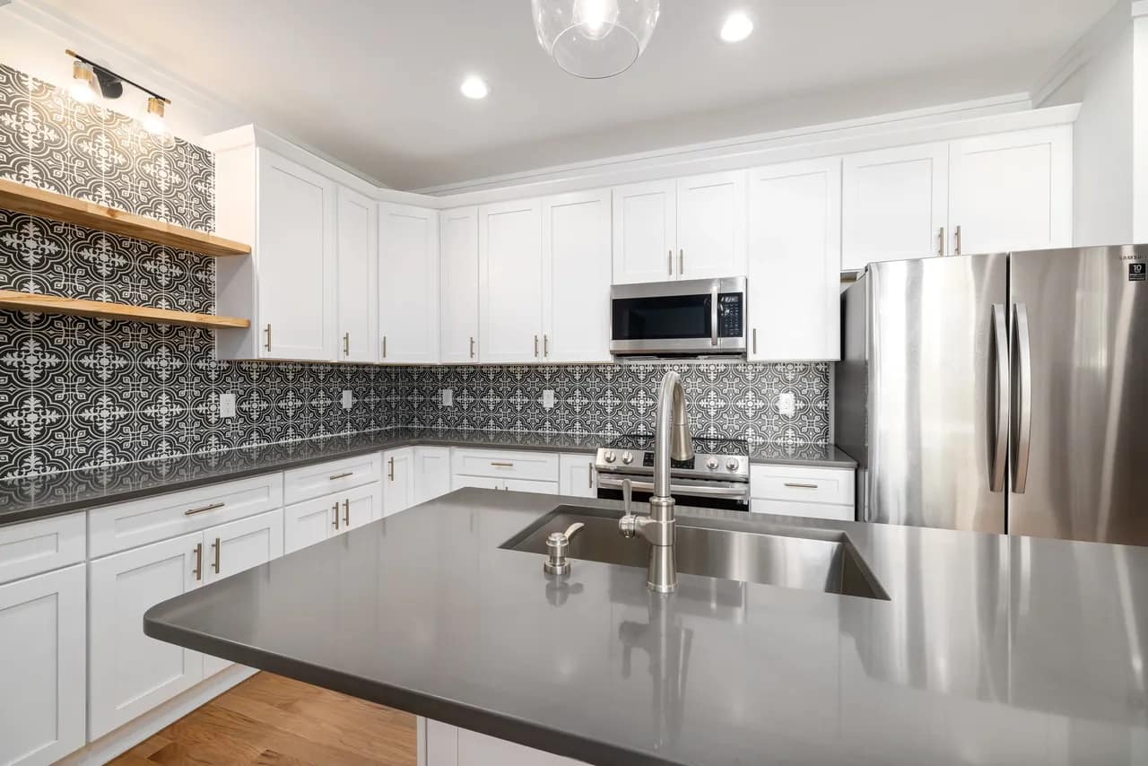 White kitchen cabinets with black backsplash tiles and wood floating shelves