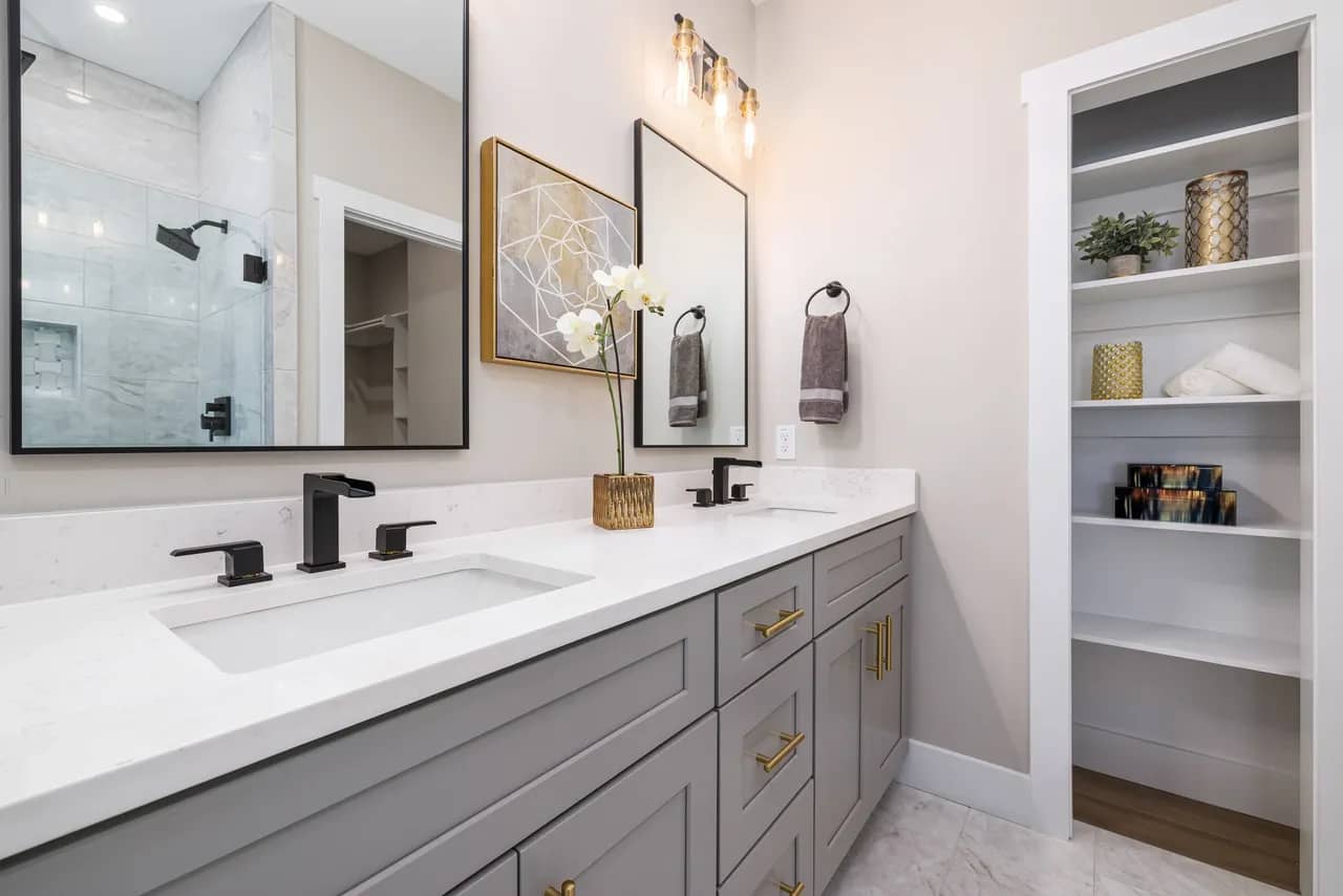 Gray bathroom vanity with gold handles and black faucets